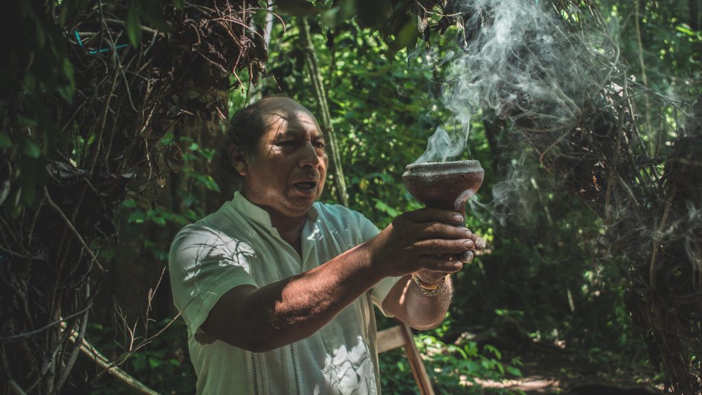 Man holding a brown pot with smoke during a Mayan ceremony in Tulum, Mexico